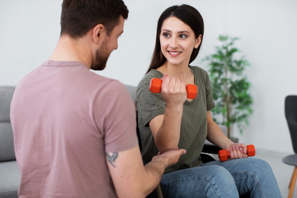 A man and a woman indoors, both smiling while holding toys. The background features a wall, and they are dressed casually.