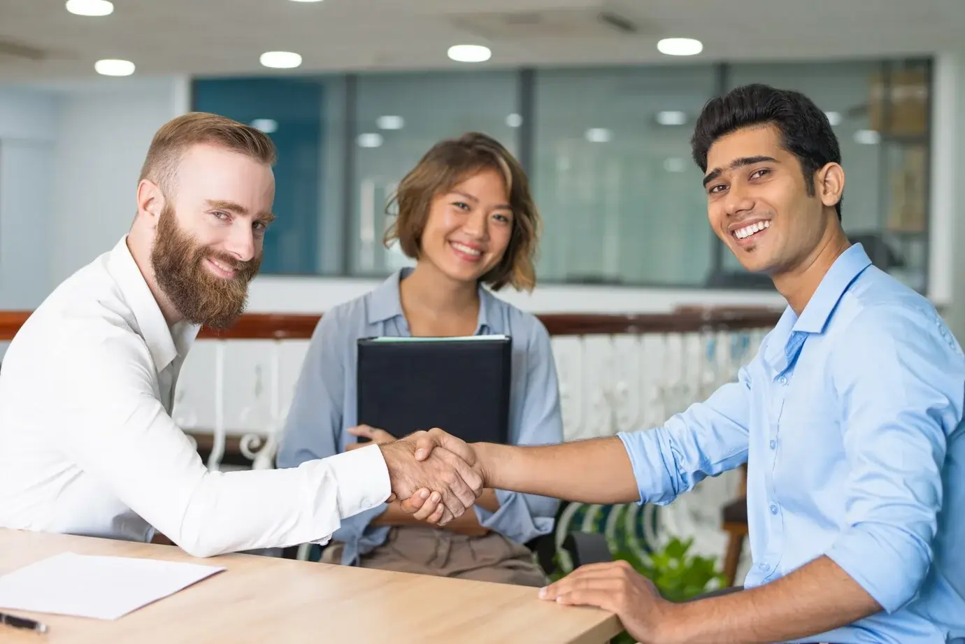 Building Strong Partnerships in Health Care A handshake between two professionals with a smiling team in the background, symbolizing collaboration and partnership in a business environment.