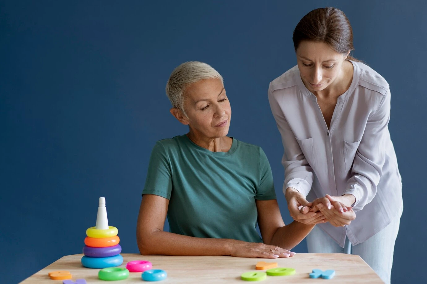 Personalized Care for Individual Well-Being A caregiver helps a senior woman with a cognitive exercise using colorful toys, offering personalized support in a calming environment.