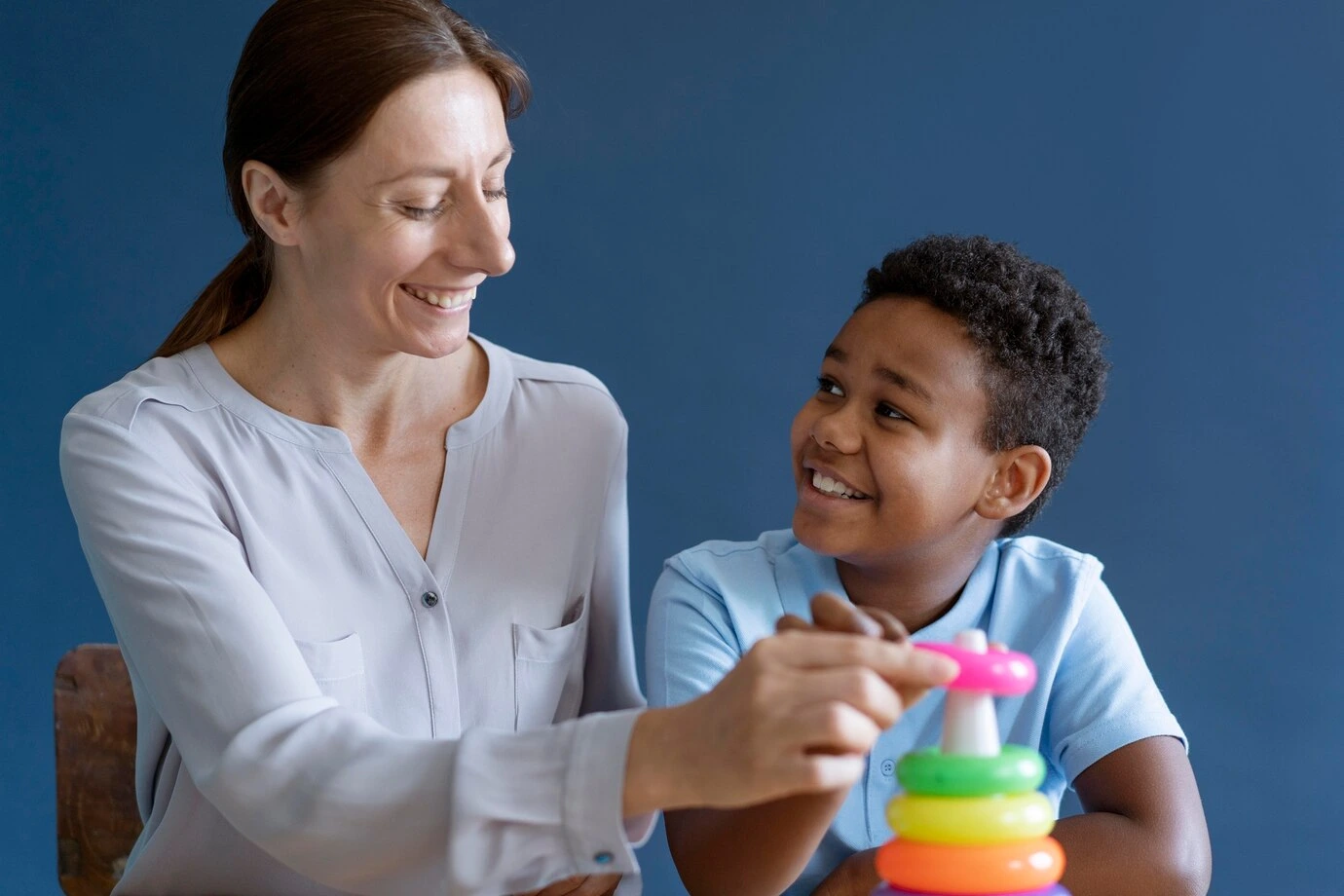 Empowering Future Generations Through Care A caregiver smiles as she assists a young boy with a stacking toy, fostering emotional well-being and growth in a supportive environment.