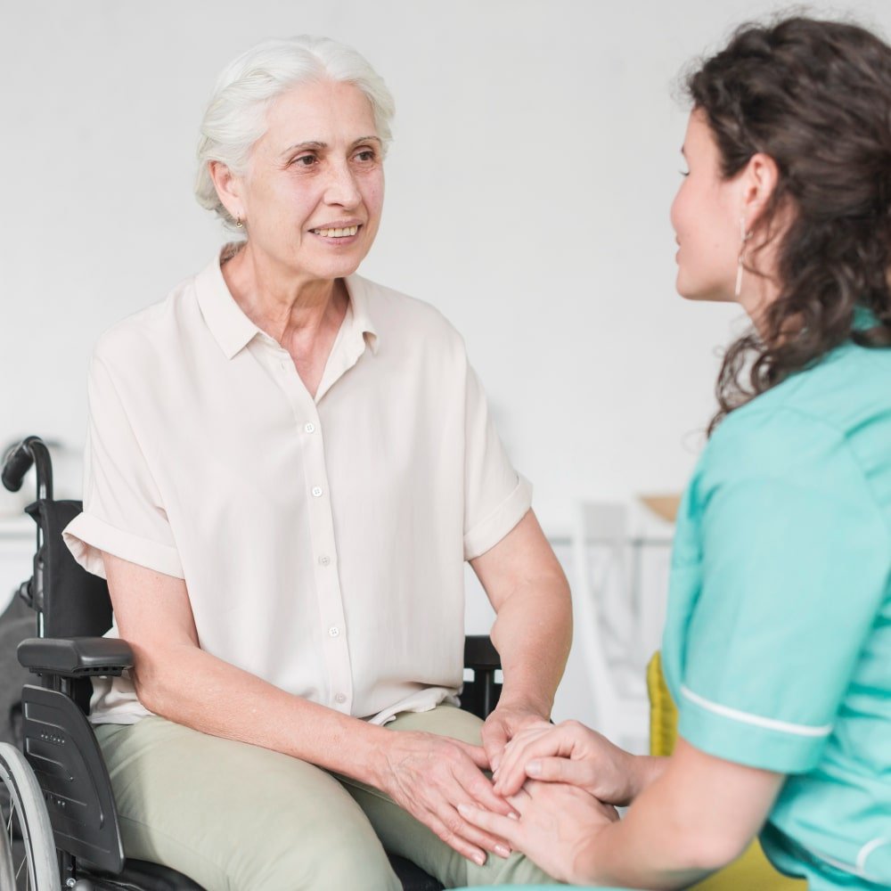 Are Looking for Temporary Adult Care Jobs? A caregiver holds hands with an elderly woman in a wheelchair, providing compassionate care in a supportive environment.