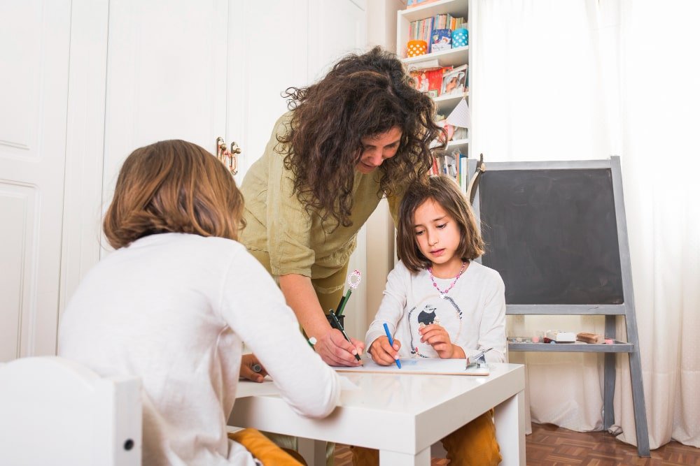 Female caregiver assisting two children with drawing at a residential care setting